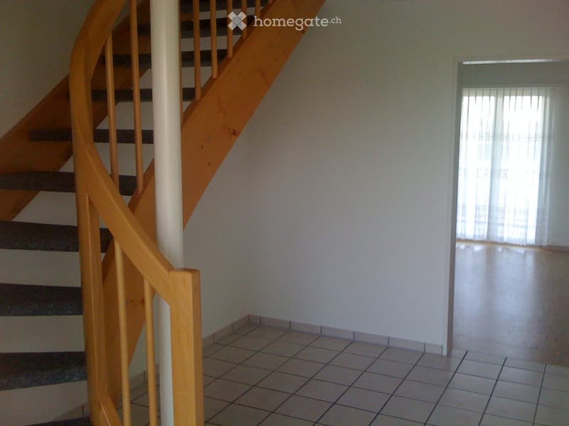 Empty hallway with tiled floor, white walls, and a wooden staircase leading upwards.