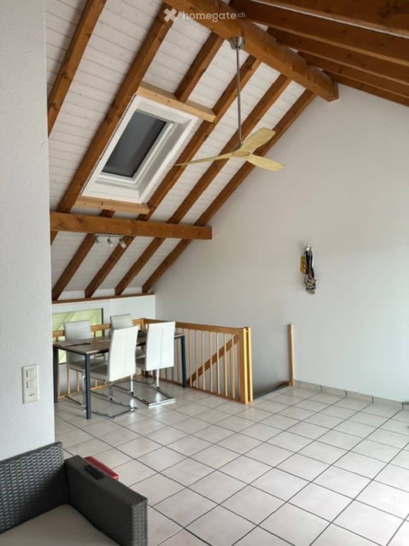 Bright attic space with wooden beams, skylight, and modern furniture including a dining table, chairs, and a sofa.