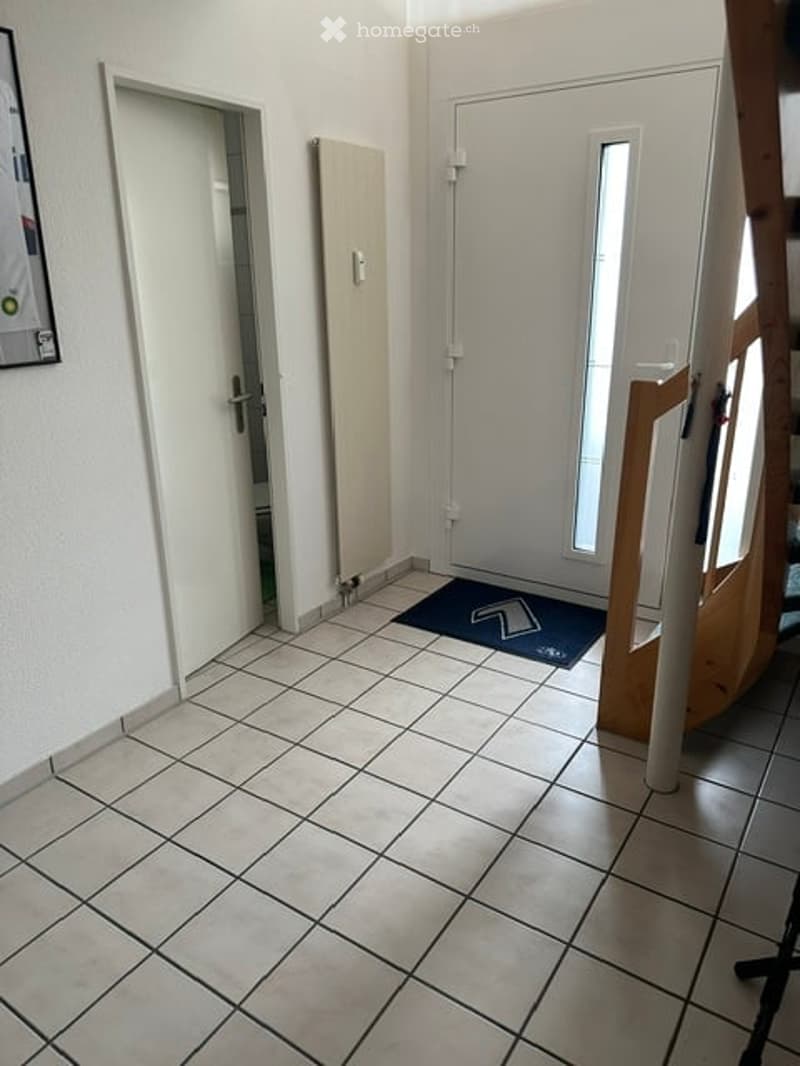 Empty hallway with tiled floor, white walls, two doors, and a small blue doormat.