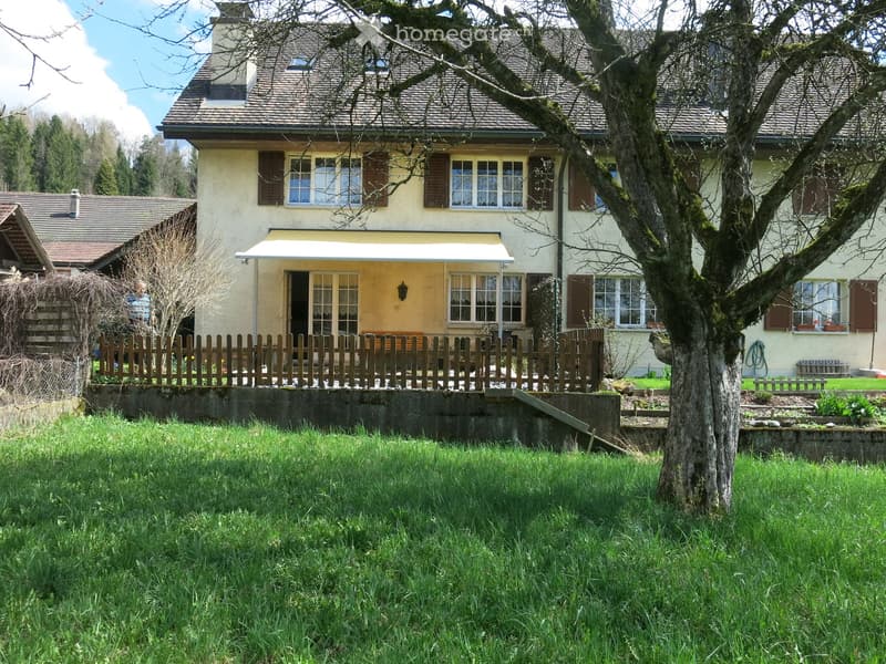 Two-story house with a beige facade, multiple windows with shutters, a covered entrance, and a wooden fence surrounding the property.