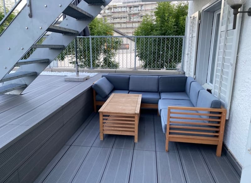 Balcony with grey decking, blue sectional sofa, wooden coffee table, and umbrella base.