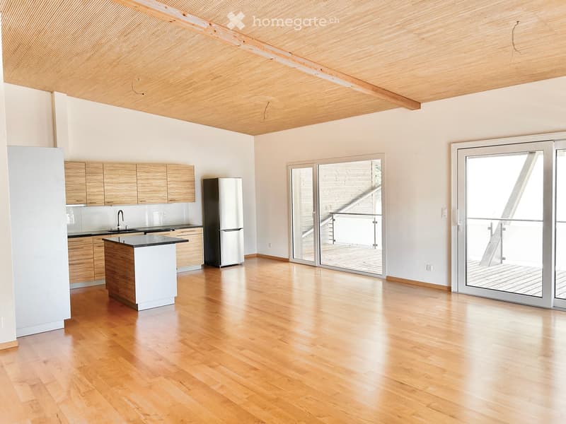 Modern kitchen with light wooden cabinets, a central island, and a stainless steel refrigerator. Large sliding glass doors lead to a balcony or outdoor area.