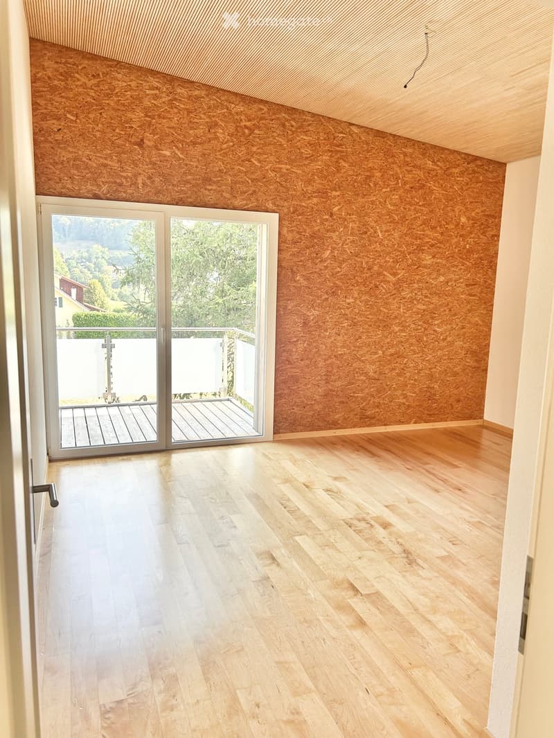 Empty room with wooden flooring, exposed wooden walls, and large sliding glass doors leading to a balcony.