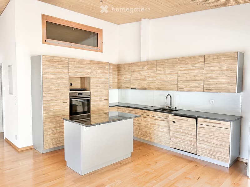 Modern kitchen with light wooden cabinets, granite countertop, and stainless steel appliances including an oven and sink.