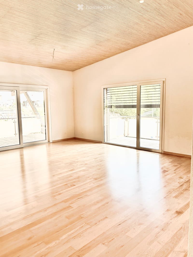 Empty room with light wooden flooring, white walls, and large sliding glass doors leading to a balcony.