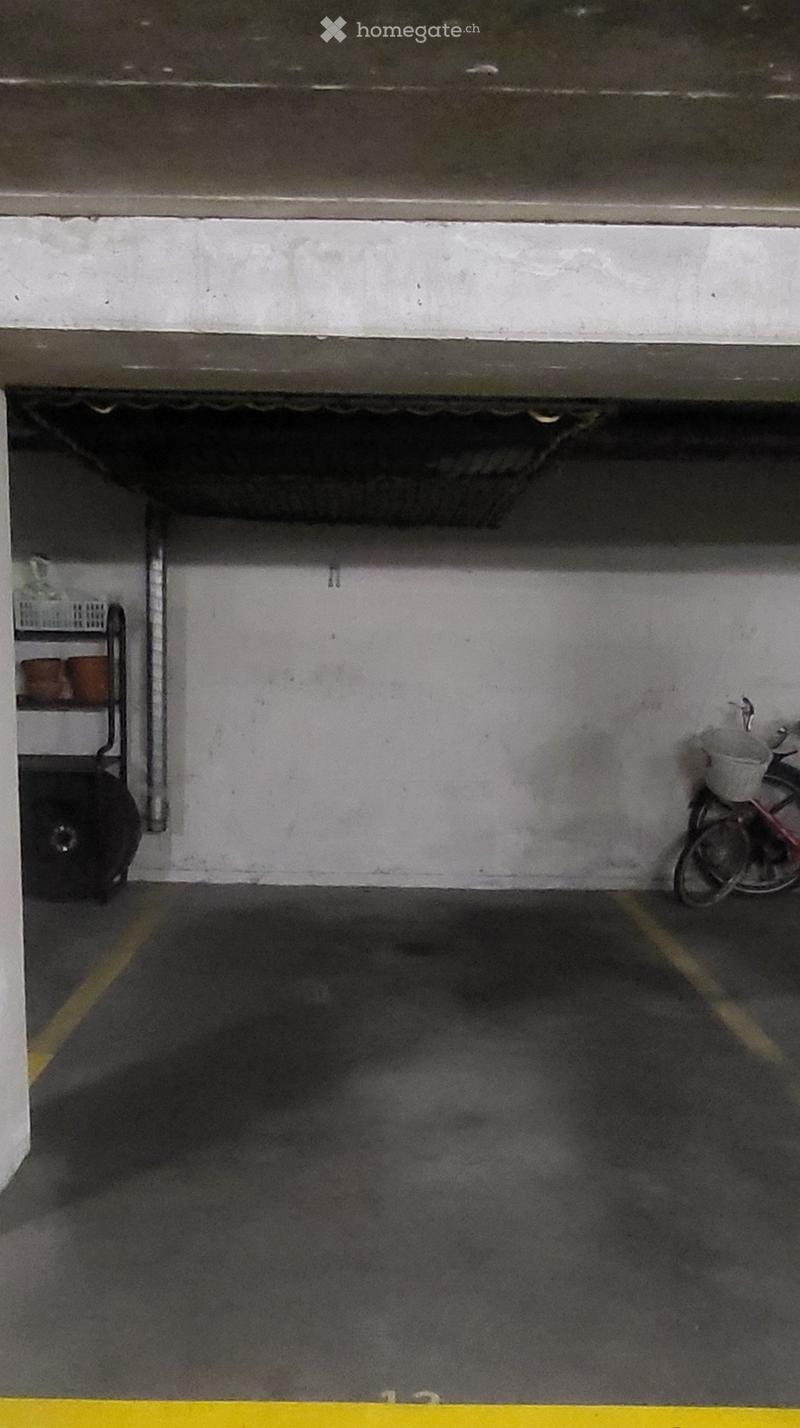 Underground garage with a single parking space, a bicycle, and a small cart with storage items.