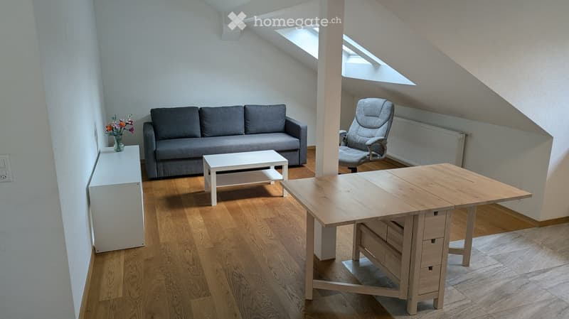 Bright living room with wooden flooring, grey sofa, white coffee table, grey armchair, and a wooden dining table with drawers.