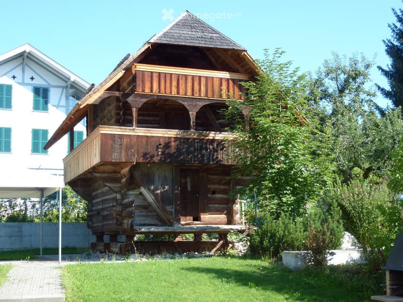 Traditional wooden house with raised ground floor, balcony, and decorative wooden architecture.