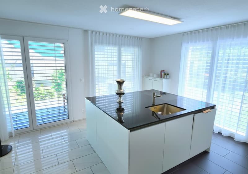 Modern kitchen with white cabinets, black countertop, stainless steel sink, and a decorative vase on the island.