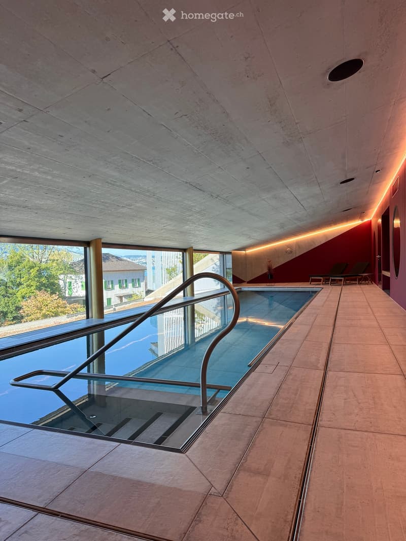 Modern indoor pool area with sleek glass railings, polished tile flooring, and contemporary lighting, overlooking a scenic outdoor view.