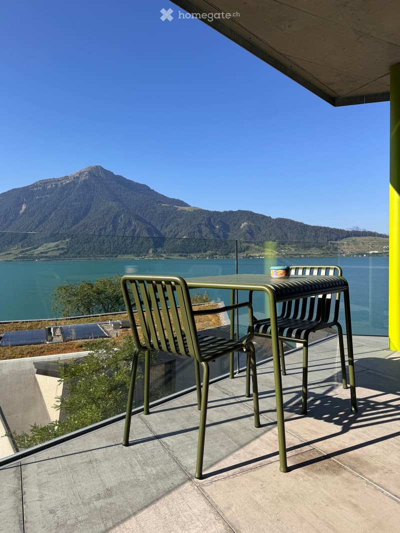 Balcony with a table and chairs, overlooking a lake and mountain range.