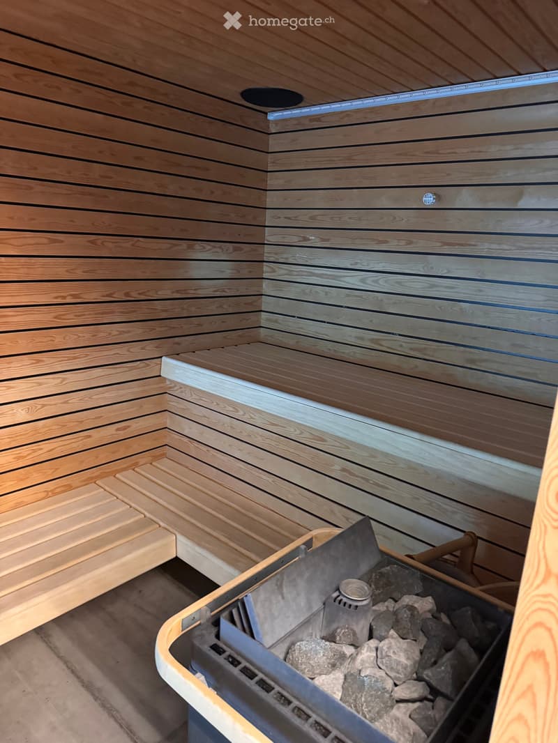 Wooden sauna interior with benches and a heater surrounded by rocks.