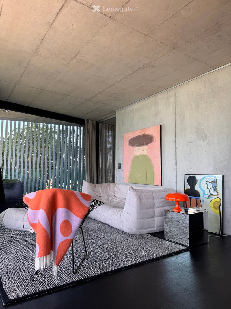 Modern living room with a white sectional sofa, side table with a lamp, abstract art pieces, and a throw blanket draped over a chair.
