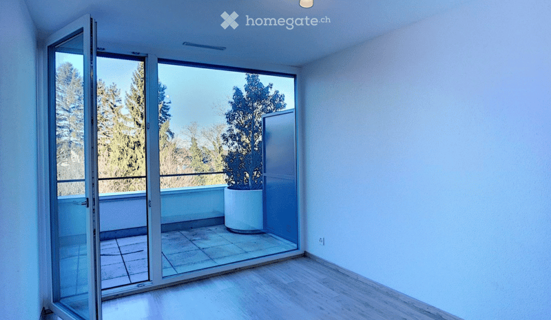 Open sliding glass doors lead to a tiled balcony with a potted plant and a view of trees.