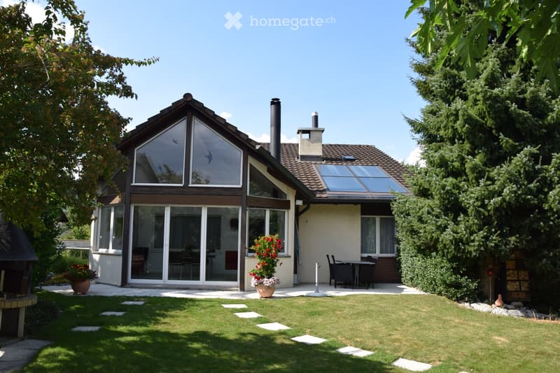 Two-story house with a modern design, large windows, and a well-maintained garden with a patio and outdoor furniture.