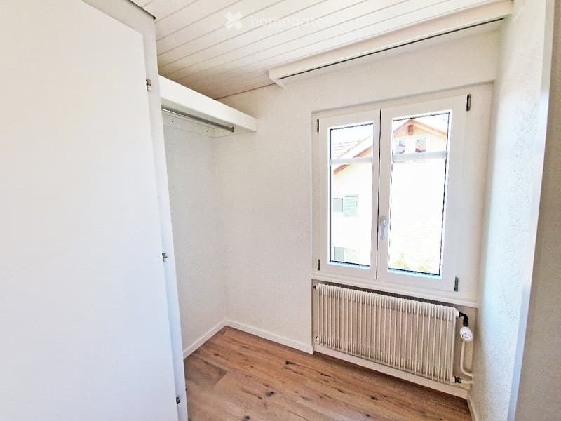 Empty room with wooden flooring, white walls, a window with double panes, a radiator, and a built-in closet with a shelf.