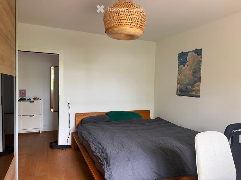 Cozy bedroom with a wooden bed, dark bedding, a hanging woven lamp, a white cabinet, and a large poster on the wall.