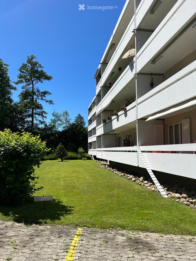 Multi-story residential building with balconies, surrounded by a well-maintained lawn and trees.