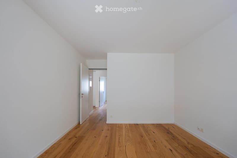 Empty room with light wooden flooring and white walls, featuring an open doorway leading to another room.