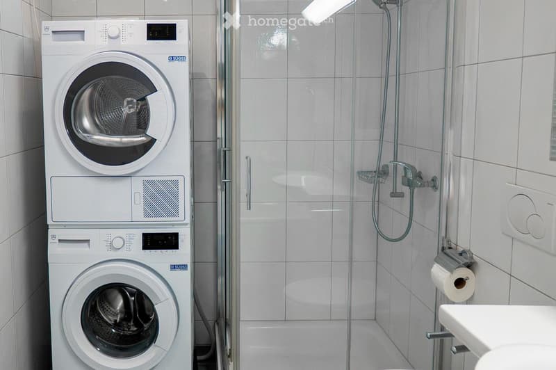 Modern bathroom with a stacked washing machine and dryer unit, a glass-enclosed shower, and a sink.