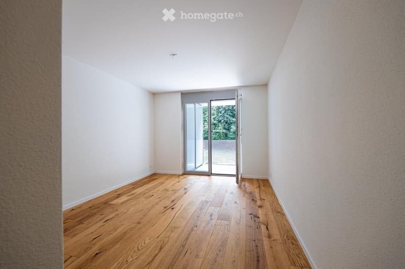 Empty room with light wooden flooring and white walls, featuring a large sliding glass door leading to an outdoor area.