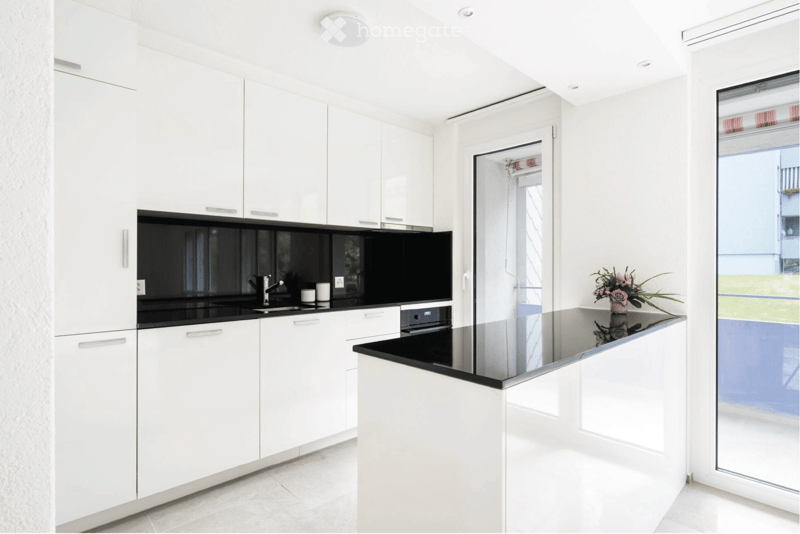 Modern kitchen with white cabinets, black countertops, a sink, and a vase with flowers on the island.