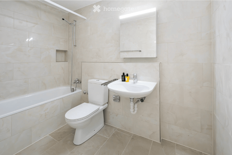 Modern bathroom with beige tiles, bathtub, toilet, sink, mirror, and showerhead.