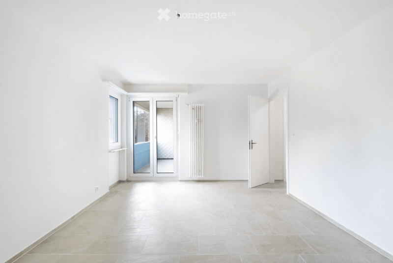 Empty room with white walls, tiled floor, large window, and sliding glass doors leading to a balcony.