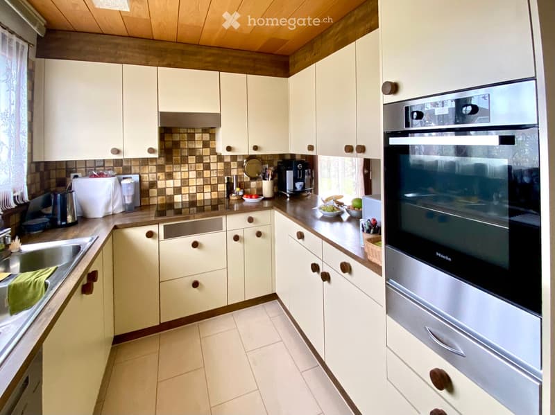 Bright kitchen with white cabinets, a stainless steel oven, and a tiled backsplash. The counter features a sink, coffee maker, and various small appliances.