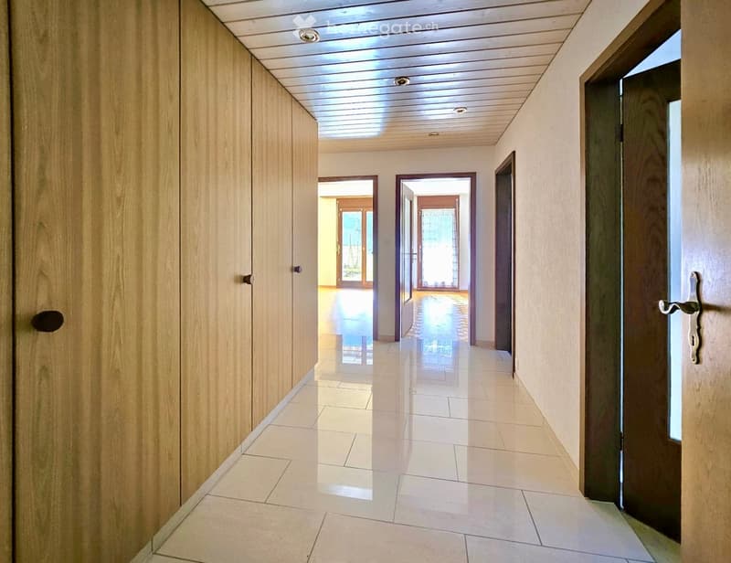 Clean, modern hallway with tiled flooring, wooden panel walls, and several doors leading to other rooms.