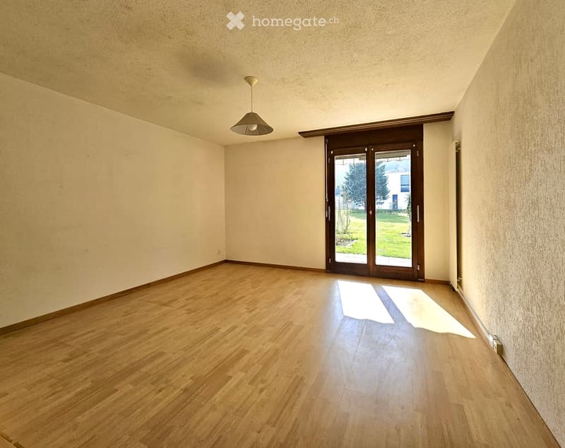 Empty room with wooden flooring, white walls, and a large sliding glass door leading to a green outdoor area.