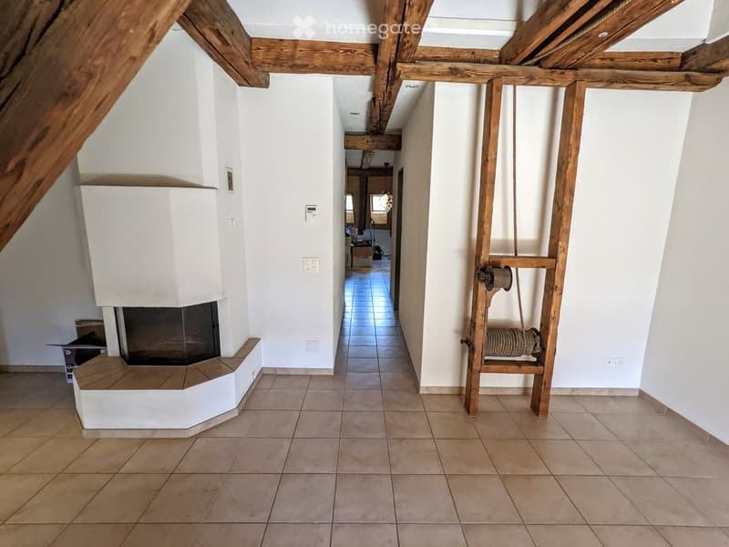 A spacious hallway with exposed wooden beams, tiled flooring, and a built-in fireplace on the left side.