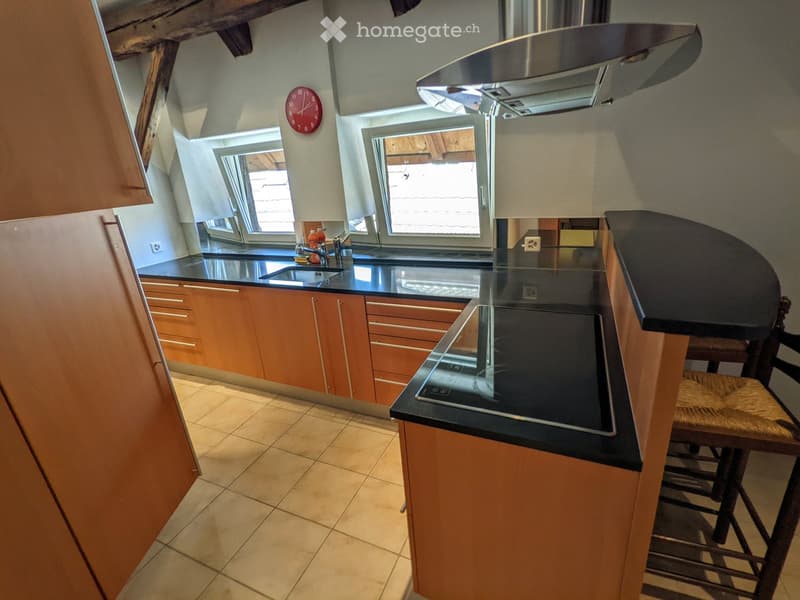 Modern kitchen with wooden cabinets, black countertops, a built-in stove, and a bar stool near the island.