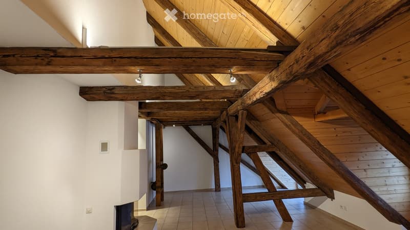 An attic corridor with exposed wooden beams and a slanted wooden ceiling, featuring recessed lighting and a tiled floor.