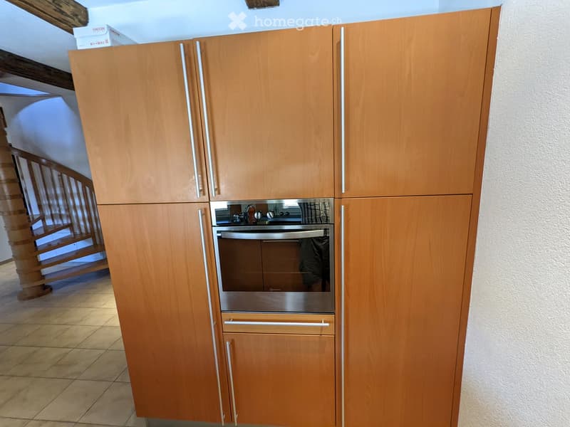 Wooden kitchen with modern cabinetry and stainless steel oven, visible in a well-lit space with tiled flooring.