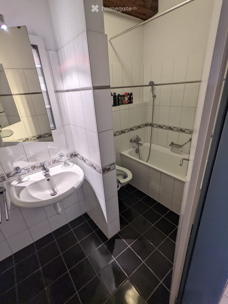 Bathroom with white tiles, dark tiled floor, sink, mirror, bathtub, toilet, and shower area.