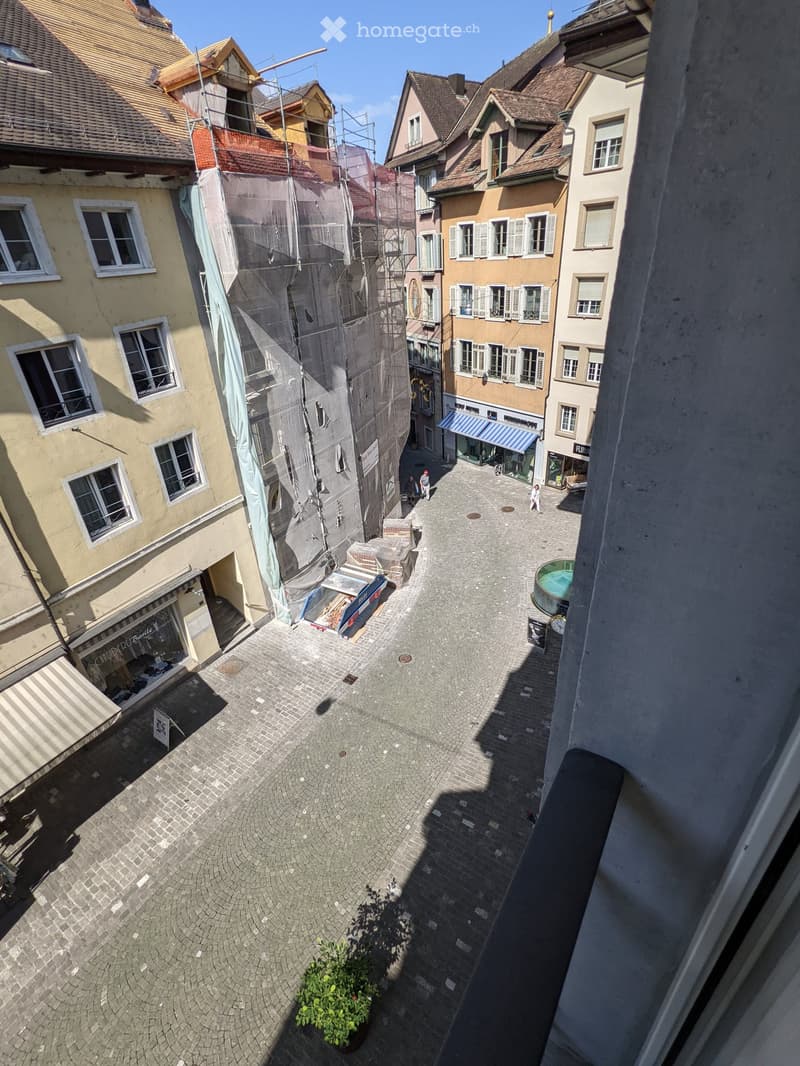 A narrow cobblestone courtyard surrounded by multi-story buildings with various architectural styles, including shops and residential units.