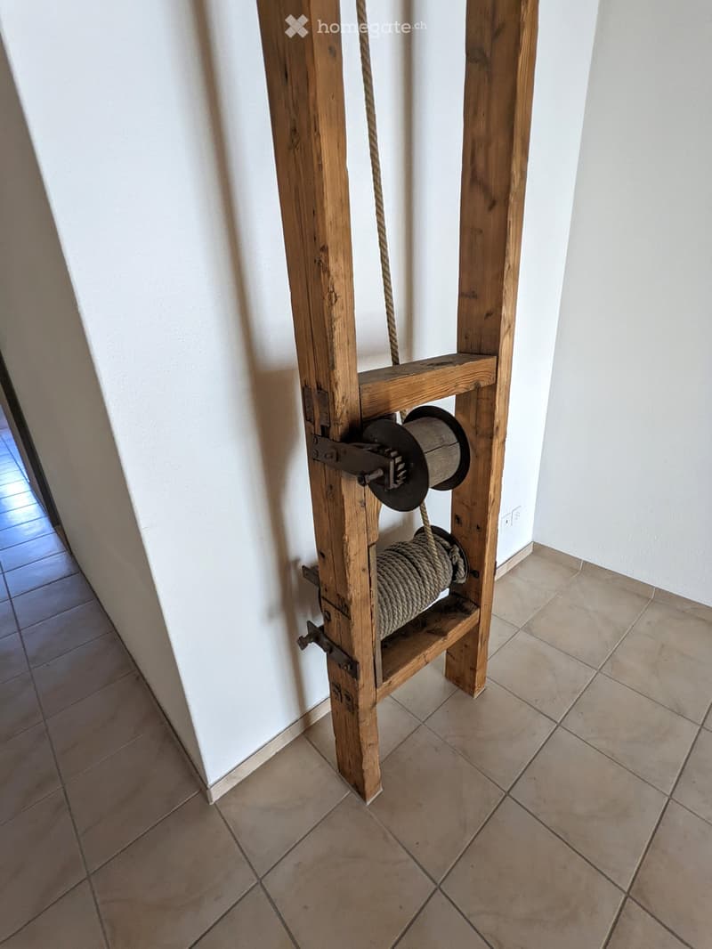 A narrow hallway with tiled flooring and white walls, featuring a wooden pulley system mounted on the wall.