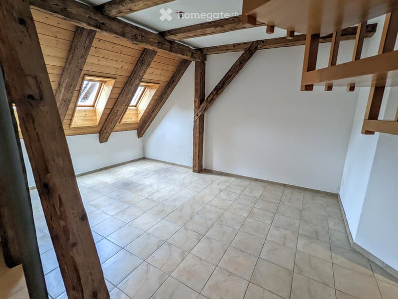 Empty attic space with exposed wooden beams, tiled floor, and skylight windows.