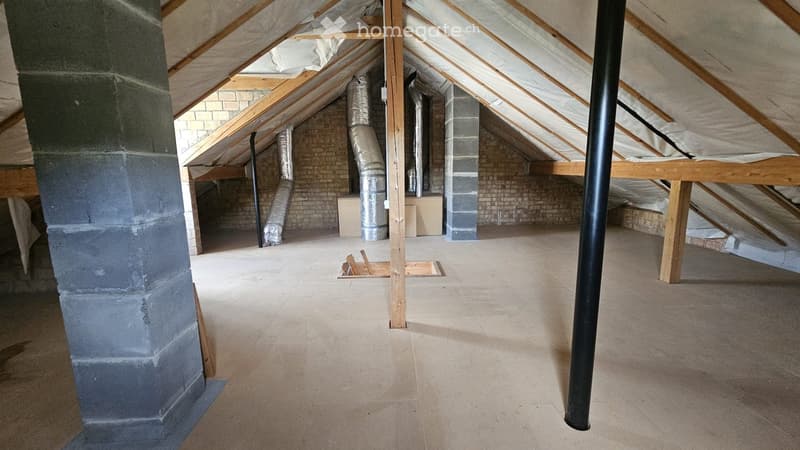 Empty attic space with exposed wooden beams, brick walls, and insulation. No furniture or equipment present.