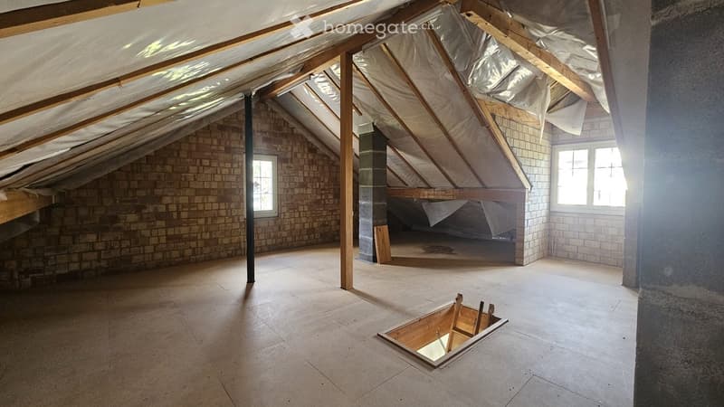 Empty attic space with exposed wooden beams, brick walls, and skylights. Features a wooden floor and a small opening in the floor.