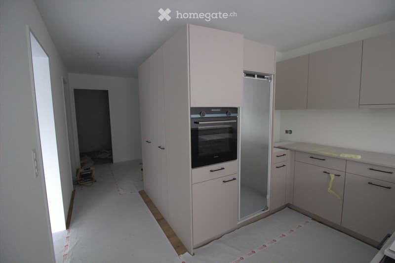Empty kitchen with light-colored cabinets, a built-in oven, and a countertop. The floor is covered with protective paper, and the space appears to be under renovation or preparation.