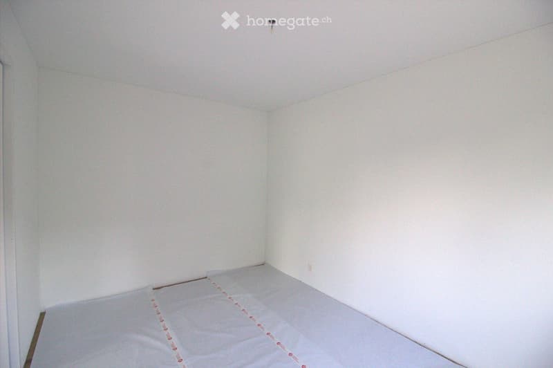 Empty room with white walls and a wooden floor, showing a mattress placed on the floor.