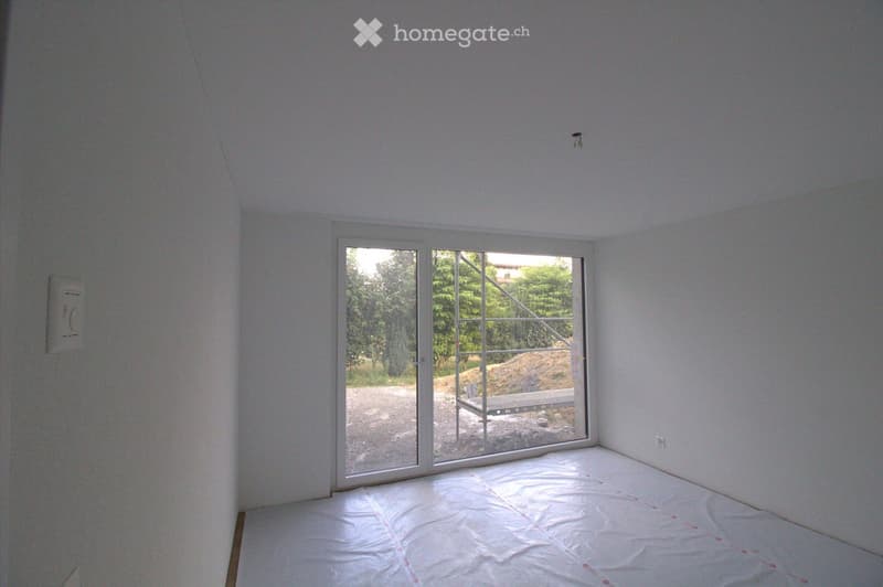 Empty room with white walls, a large glass sliding door leading to an outdoor area, and a protective plastic sheet covering the floor.