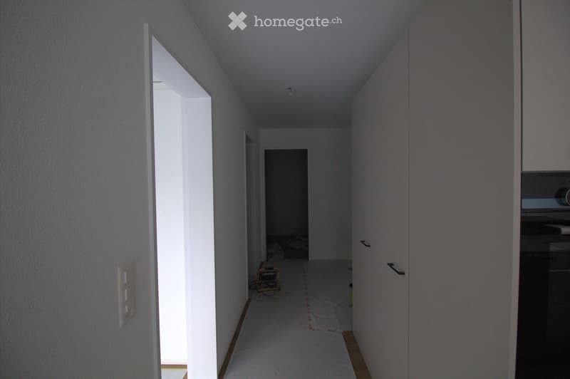 Empty hallway with white walls, wooden flooring, and a partially open door leading to another room.