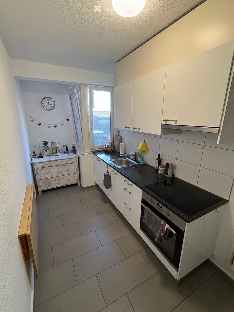 Modern kitchen with white cabinets, black countertops, and stainless steel appliances. Features include a sink, coffee maker, and built-in oven.