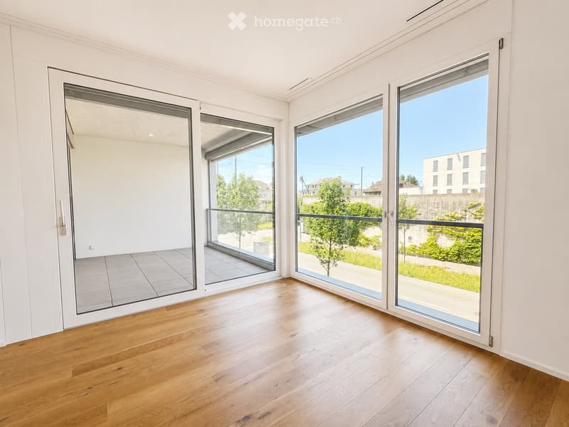 Bright, empty room with wooden flooring, large glass sliding doors leading to a balcony, and white walls.