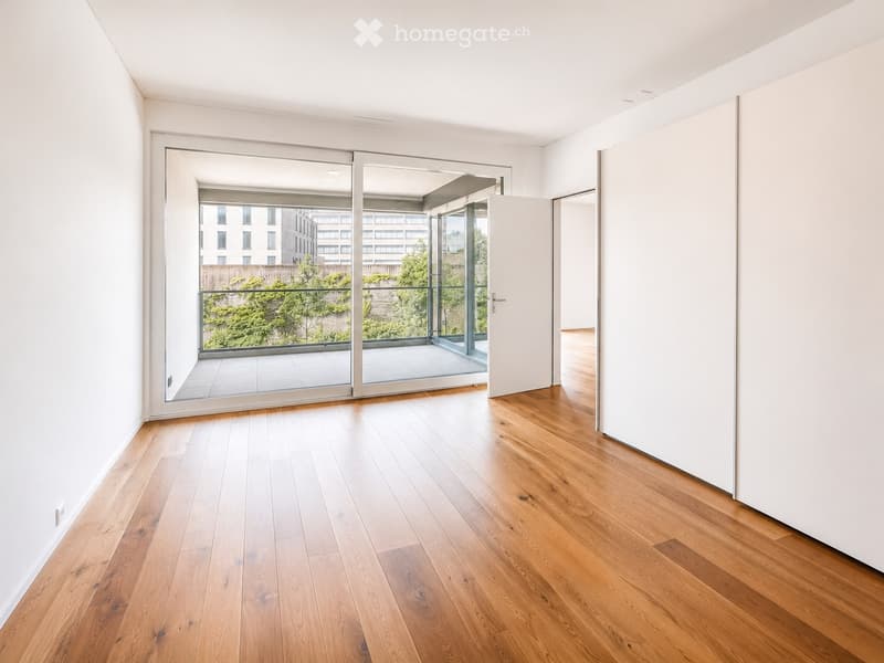 Bright, unfurnished room with wooden flooring, white walls, and large sliding glass doors leading to a balcony.