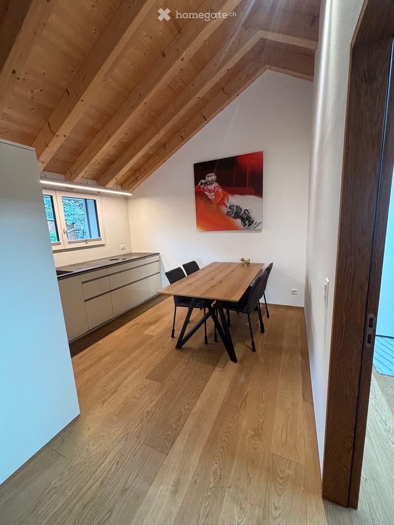 Modern dining area with wooden floor, sleek kitchen cabinetry, and a large painting on the wall.