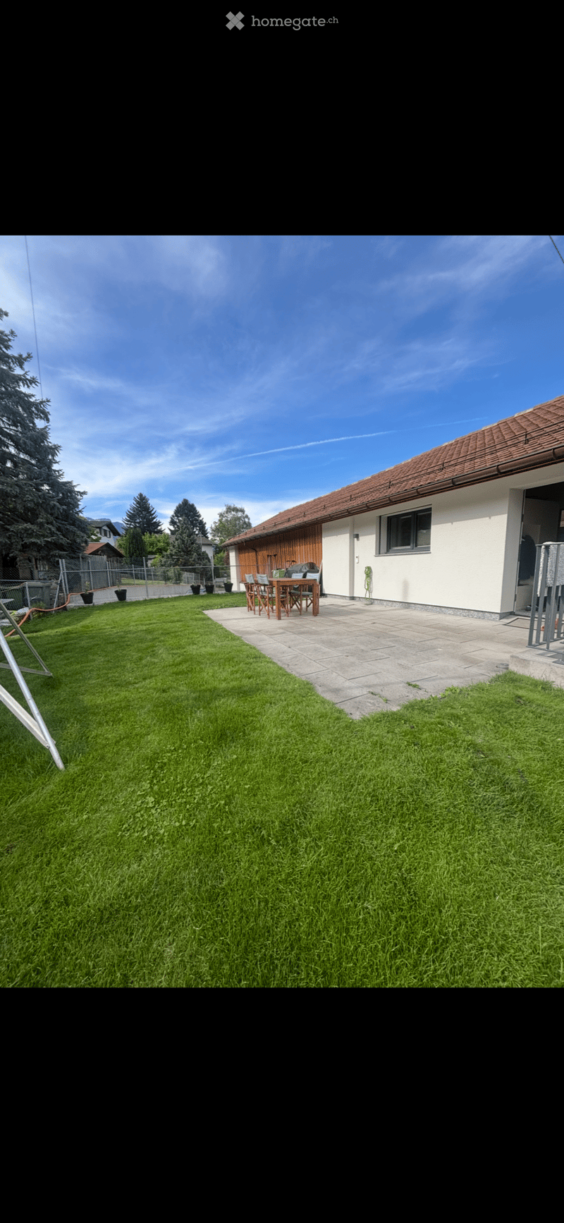 Well-maintained garden with a neatly trimmed lawn, a paved patio area, and a wooden table with chairs near the house.